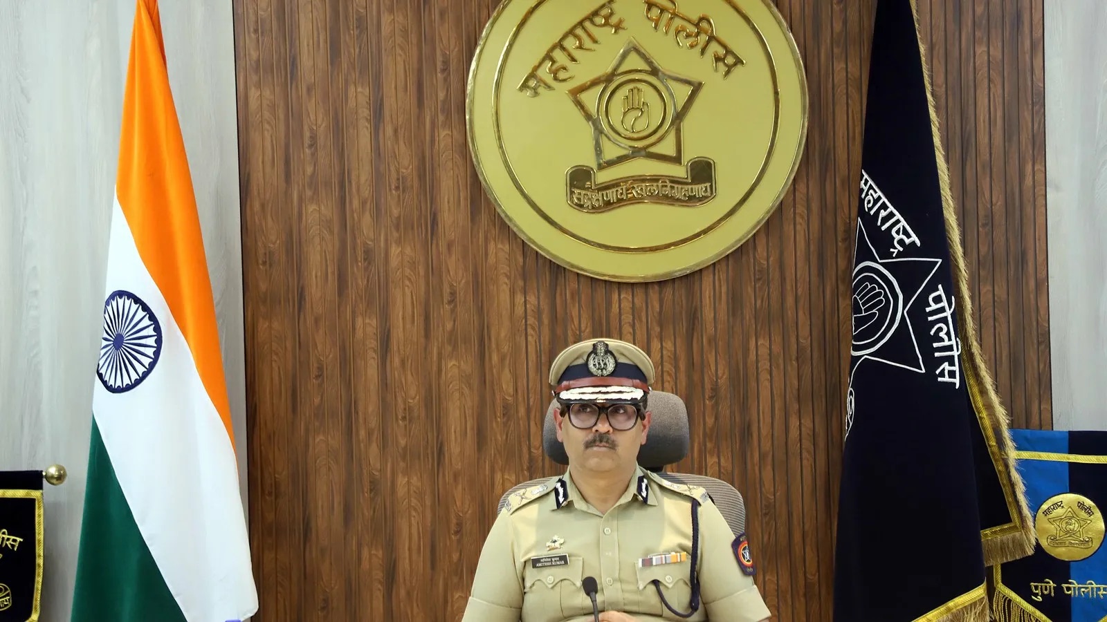 Amitesh Kumar seated at the commissioner's desk beneath the Maharashtra Police emblem, with the national flag and departmental standards