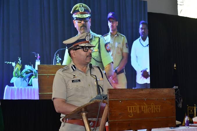 Amitesh Kumar speaking from a Pune Police lectern at a community programme, a presentation screen behind him